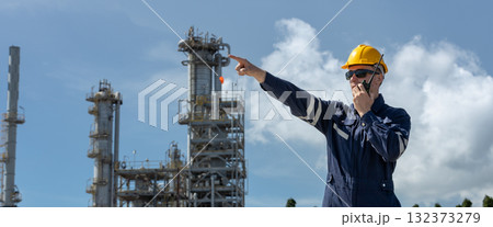 Industrial engineer with radio pointing at refinery facility, demonstrating leadership, supervision, and communication in oil and gas operations. 132373279