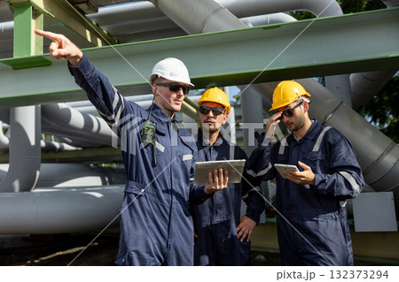 Team of industrial engineers wearing safety helmets using tablet and walkie-talkie at construction site, representing teamwork, engineering planning, refinery inspection and site supervision. Team of industrial engineers wearing safety helmets using tablet and walkie-talkie at construction site, representing teamwork, engineering planning, refinery inspection and site supervision. 132373294