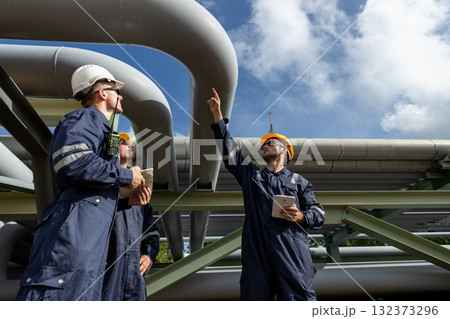 Team of industrial engineers wearing safety helmets using tablet and walkie-talkie at construction site, representing teamwork, engineering planning, refinery inspection and site supervision. 132373296