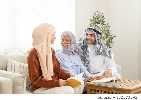 Three muslim family members in warm inviting living room Everyone dresses in lifestyle of Middle Eastern Arabs. They share smiles and holding book learning strengthen relationships within home. 132373342