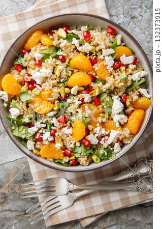 Vegetarian quinoa salad with fresh spinach, feta, tangerines, pomegranate and pistachios close-up in a bowl on the table. Vertical top view 132373915