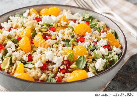 Diet quinoa salad with spinach, feta, tangerines, pomegranate, and pistachios dressed with a lemon-yogurt sauce, close-up in a bowl. Horizontal 132373920