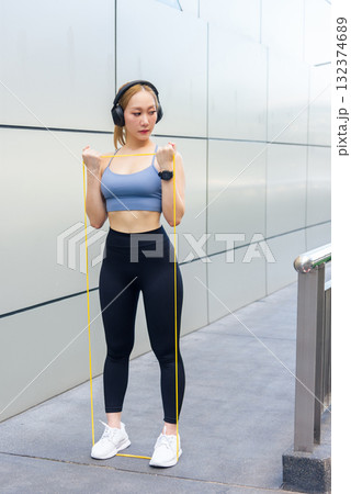 Fit woman performs sport exercise workout outdoor, using resistance band for arm stretch, developing fit physique, people pursue fitness goals 132374689