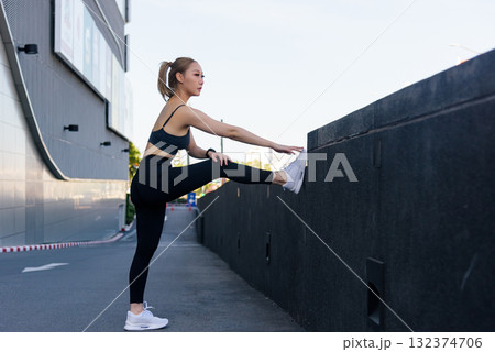 Fit sport woman performs outdoor workout, people stretch for exercise achieving leg flexibility and good body stretch routine with dedication for overall health 132374706