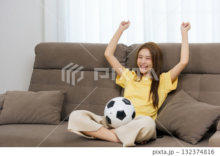 Young woman happy at home people enjoy activity watching football game on comfortable couch celebrating team goal with arms raised joyful leisure entertainment Young woman happy at home people enjoy activity watching football game on comfortable couch celebrating team goal with arms raised joyful leisure entertainment 132374816