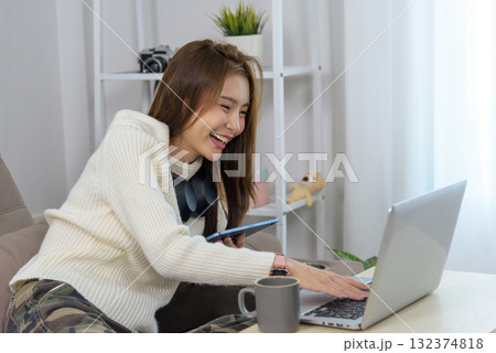 Young happy woman engages in home activity, people connect using laptop, smartphone, enjoying remote work, online learning, or entertainment, smiling broadly with headphones on neck Young happy woman engages in home activity, people connect using laptop, smartphone, enjoying remote work, online learning, or entertainment, smiling broadly with headphones on neck 132374818