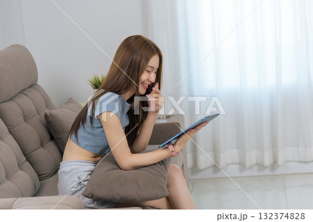 Young happy woman at home enjoying casual activity, people find joy with modern technology, she relaxes comfortably on couch, engaging with digital tablet, feeling cheerful and connected Young happy woman at home enjoying casual activity, people find joy with modern technology, she relaxes comfortably on couch, engaging with digital tablet, feeling cheerful and connected 132374828