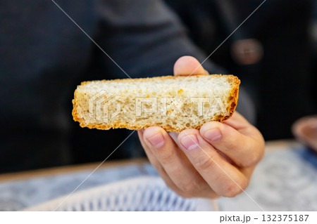Freshly baked bread slice held by a person in a warm dining setting during a casual gathering. white wheat pan bread 132375187