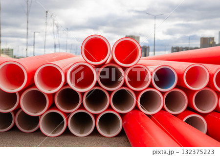 Bright red conduit plastic pipes stacked neatly on a construction site. close-up view 132375223