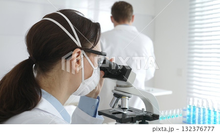 Two scientists, a man and a woman, in lab coats and protective gear, conduct research in a sterile laboratory. Concept of medicine and science Two scientists, a man and a woman, in lab coats and protective gear, conduct research in a sterile laboratory. Concept of medicine and science 132376777