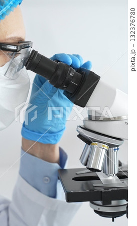 Scientist woman wearing gloves and a mask uses a microscope in a laboratory setting, conducting important research and analysis, close up. Medicine and science concept 132376780