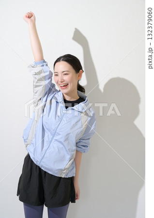 白背景でガッツポーズをするスポーツウェアの女性 132379060