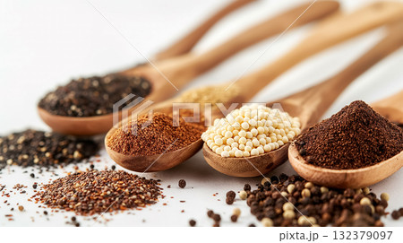 Assorted spices including pepper and mustard seeds on wooden spoons against a white background, symbolizing culinary diversity. 132379097