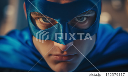 Intense gaze of a young person dressed as a superhero with a blue mask and cape, embodying strength and vigilance. 132379117