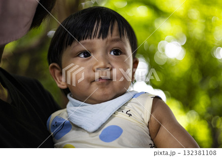 Toddler Mesmerized By Night Lights In Mother Arms, A captivated toddler stares at night lights from mother arms, eyes aglow in the dark, perfect for family photo shot or a magical moment showcase. 132381108