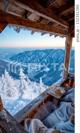 The winter vacation chalet features a warm interior with blankets and drinks, showcasing breathtaking mountain views enveloped in a serene snow-covered landscape 132381160