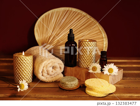 Still life of spa accessories with rolled towels, natural soaps, oils and candles on wooden surface. Warm lighting highlighting textures and neutral tones for wellness and aromatherapy visuals Still life of spa accessories with rolled towels, natural soaps, oils and candles on wooden surface. Warm lighting highlighting textures and neutral tones for wellness and aromatherapy visuals 132383477