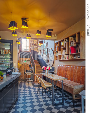 Warm and eclectic interior of a lobby bar with striking checkerboard floor and a cluster of modern pendant lights overhead. Cozy, lived-in atmosphere of modern design with rustic elements 132383887