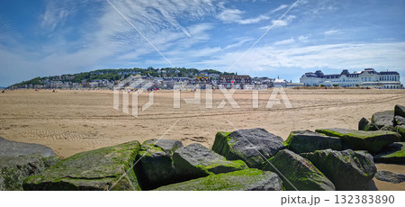 Panoramic view of Trouville-sur-Mer sandy beach, Normandy, France. Large, moss-covered breakwater rocks in foreground and charming town with traditional buildings in the background Panoramic view of Trouville-sur-Mer sandy beach, Normandy, France. Large, moss-covered breakwater rocks in foreground and charming town with traditional buildings in the background 132383890