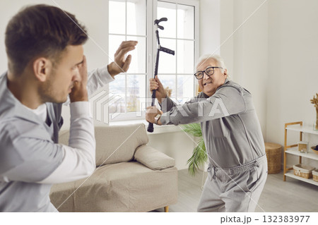 Angry exasperated senior man going to hit young male caregiver or nurse with his crutch Angry exasperated senior man going to hit young male caregiver or nurse with his crutch 132383977