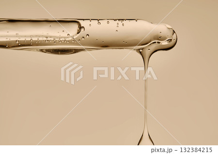 The texture of the serum flowing out of the pipette on a beige background. 132384215