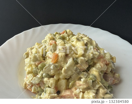 Olivier salad on a white plate. A homemade salad with meat, boiled vegetables, eggs, and mayonnaise. 132384580