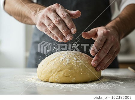 Close-up of a baker's hands sprinkling flour on fresh dough. A man preparing homemade bread in the kitchen. Culinary food preparation process 132385005