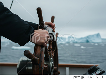 A person's hands steering a ship's wooden wheel in a polar sea. Navigating through icebergs on an arctic expedition. Adventure and exploration concept 132385131