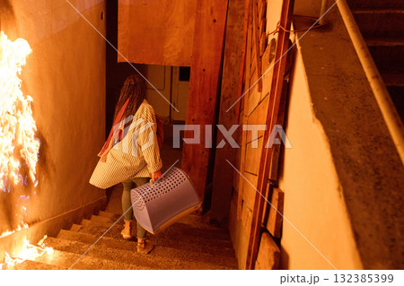Woman escaping fire with pet carrier, running down stairs in emergency, indoor scene, danger concept, risk and safety, action shot, dramatic lighting, real life situation, hope, fear. Woman escaping fire with pet carrier, running down stairs in emergency, indoor scene, danger concept, risk and safety, action shot, dramatic lighting, real life situation, hope, fear. 132385399