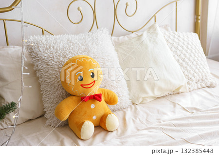 Cozy bedroom with cheerful gingerbread plush toy sitting on bed with decorative pillows Cozy bedroom with cheerful gingerbread plush toy sitting on bed with decorative pillows 132385448