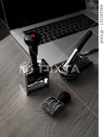 Metal office stamps on desk with laptop in background - vertical photo 132385569