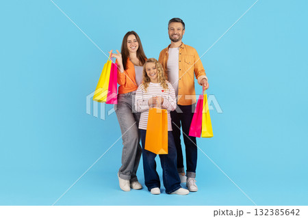 Cheerful family standing together with colorful shopping bags on blue studio background Cheerful family standing together with colorful shopping bags on blue studio background 132385642