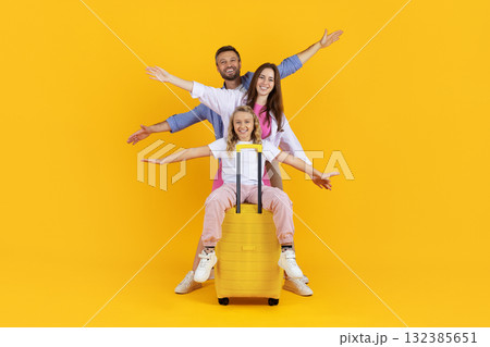 Happy parents and daughter with big suitcase having fun on yellow background Happy parents and daughter with big suitcase having fun on yellow background 132385651