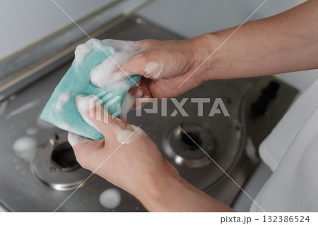 Cleaning company worker squeezing soapy water from sponge during cleaning dirty gas stove, to removing grime, grease, promoting hygiene, cleanliness in kitchen. Concept of domestic work, household. Cleaning company worker squeezing soapy water from sponge during cleaning dirty gas stove, to removing grime, grease, promoting hygiene, cleanliness in kitchen. Concept of domestic work, household. 132386524