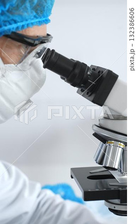 Medical scientist senior man wearing protective mask, glasses and bouffant cap using microscope doing scientific research in a laboratory. Medicine and science concept 132386606