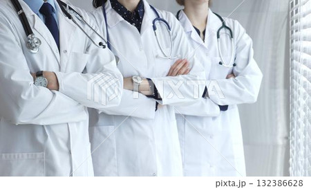 Doctors in white uniforms with stethoscopes stand together with folded hands, symbolizing unity, competence, experience, and dedication to the healthcare profession 132386628