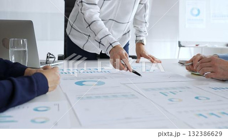 Business team analyzing financial charts and data reports during strategy meeting, hands pointing to documents on table with graphs and diagrams for planning 132386629