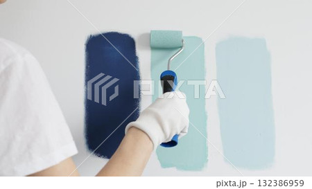 Painter wearing protective gloves rolling blue paint on white wall, creating gradient color effect for home interior renovation project 132386959