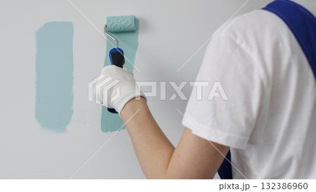 Professional painter holding paint roller, comparing light green paint shades, selecting precise wall color for home renovation, ensuring ideal interior design aesthetic 132386960