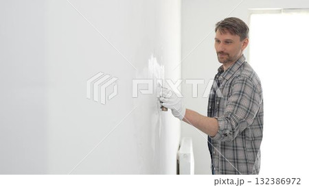 Construction worker spreading plaster on white wall, wearing protective gloves and t-shirt during home renovation project, working with professional skill and focus Construction worker spreading plaster on white wall, wearing protective gloves and t-shirt during home renovation project, working with professional skill and focus 132386972