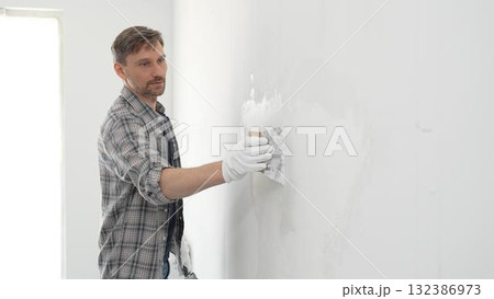 Construction worker spreading plaster on white wall, wearing protective gloves and t-shirt during home renovation project, working with professional skill and focus Construction worker spreading plaster on white wall, wearing protective gloves and t-shirt during home renovation project, working with professional skill and focus 132386973