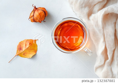 Warm Herbal Tea in Glass Cup with Autumn Leaves and Soft Fabric on Light Background 132387881