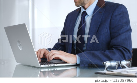Professional businessman working on laptop computer, typing on keyboard at modern office desk, managing business tasks. Business people concept 132387960