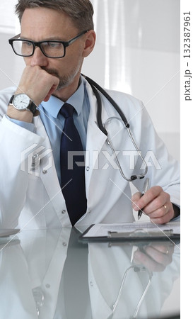 Male doctor in lab coat and stethoscope working on laptop, providing medical consultation in a modern clinic office. Medicine and health care Male doctor in lab coat and stethoscope working on laptop, providing medical consultation in a modern clinic office. Medicine and health care 132387961