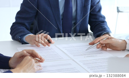 Business people or lawyers reviewing and discussing contract while gathering in a bright office around a desk strewn with legal documents and pens Business people or lawyers reviewing and discussing contract while gathering in a bright office around a desk strewn with legal documents and pens 132388084