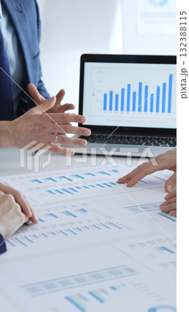 Business professionals collaborating at a table, discussing financial data and reports with a calculator and laptop displaying charts, focusing on strategy and planning Business professionals collaborating at a table, discussing financial data and reports with a calculator and laptop displaying charts, focusing on strategy and planning 132388115