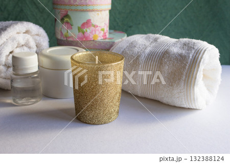 A golden candle in the foreground , white towels, and spa items in an aesthetic arrangement.Horizontal shot. Natural light A golden candle in the foreground , white towels, and spa items in an aesthetic arrangement.Horizontal shot. Natural light 132388124