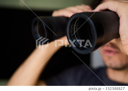 A person using binoculars to observe their surroundings with great focus and detail A person using binoculars to observe their surroundings with great focus and detail 132388827
