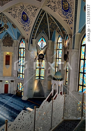 The bright, high-ceilinged interior of the Kul Sharif Mosque with ornate white railings and worshippers on the blue carpet. 132389337