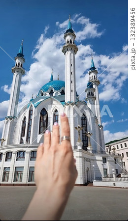 The grand white and blue Kul Sharif Mosque under a sunny sky, with a person's hand reaching towards a minaret. The grand white and blue Kul Sharif Mosque under a sunny sky, with a person's hand reaching towards a minaret. 132389456